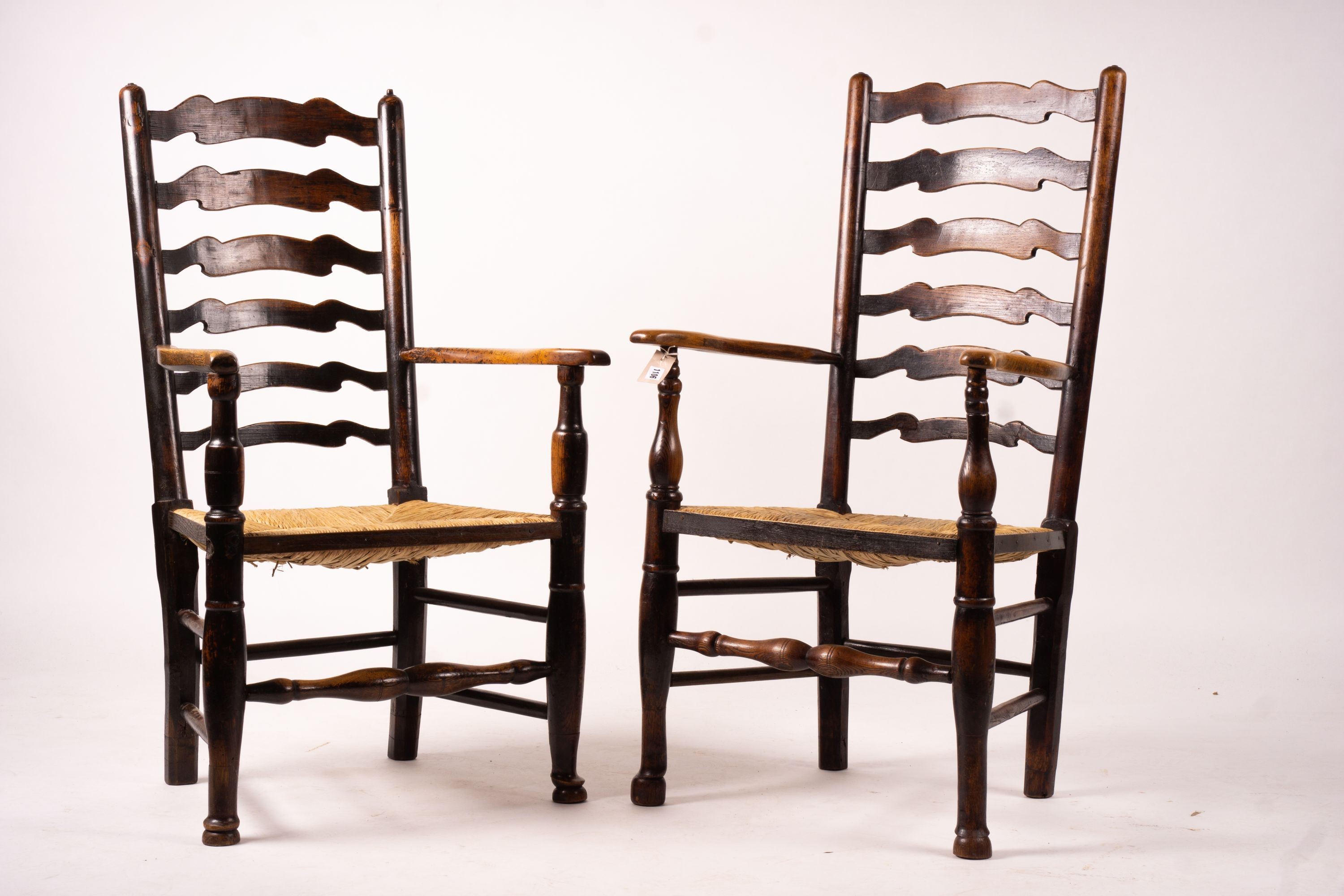 A pair of early 19th century Lancashire ash and fruitwood rush seat ladderback elbow chairs, width 60cm, depth 46cm, height 110cm